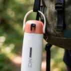 White insulated bottle hanging from a bag strap outdoors
