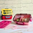 Lunch boxes in yellow red and pink with cutlery sets
